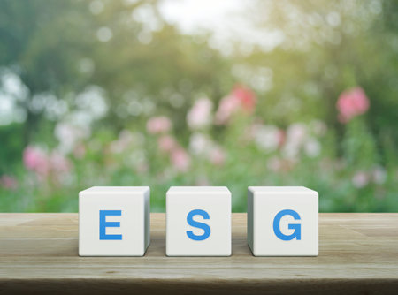 ESG acronym on white block cubes on wooden table over blur pink flower and tree in garden, Environmental Social Corporate Governance conceptの写真素材