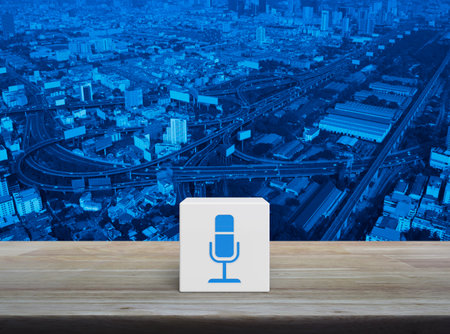 Microphone flat icon on white block cube on wooden table over modern city tower, street, expressway and skyscraper, Technology communication conceptの写真素材