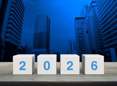 2026 letter on white block cubes on wooden table over modern office city tower and skyscraper, Happy...