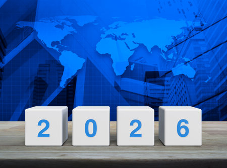 2026 letter on white block cubes on wooden table over world map, modern office city tower and...