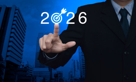 Businessman pressing 2026 letter with goal flat icon over modern office city tower and skyscraper,...