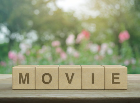 Movie letter on wood block cubes on wooden table over blur pink flower and tree in garden, Business cinema online conceptの写真素材