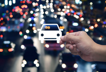 Hand holding car flat icon in fingers over blur colourful night light traffic jam road in city, Business transportation service conceptの写真素材