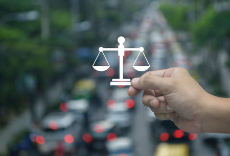 Hand holding law flat icon in fingers over blur of rush hour with cars and road in city, Business legal service conceptの写真素材