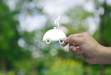 Hand holding restaurant cloche flat icon in fingers over blur green tree in park, Food delivery online service conceptの写真素材