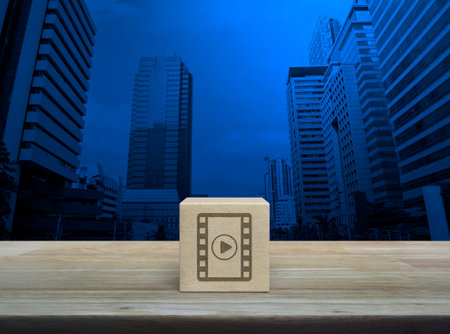 Play button with movie flat icon on wood block cube on wooden table over modern office city tower and skyscraper, Business cinema online conceptの写真素材