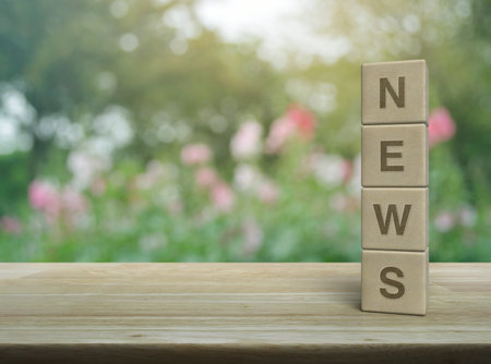 NEWS letter on wood block cubes on wooden table over blur pink flower and tree in park, Business communication conceptの写真素材