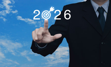 Businessman pressing 2026 letter with goal flat icon over blue sky with white clouds, Business happy new year 2026 success conceptの写真素材