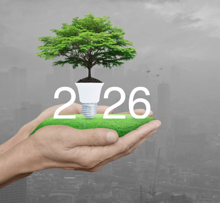 2026 white text with fresh big tree on soil and light bulb on green grass in hands over pollution of...