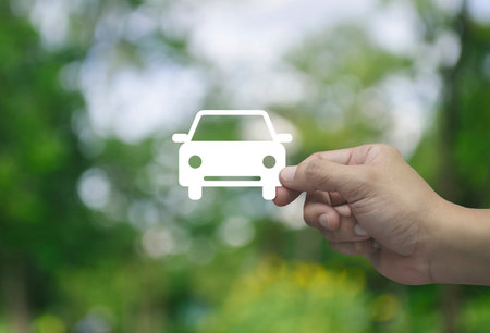 Hand holding car flat icon in fingers over blur green tree in park, Business transportation service conceptの写真素材