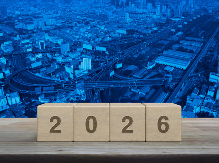 2026 letter on wood block cubes on wooden table over modern city tower, street, expressway and skyscraper, Happy new year 2026 cover conceptの写真素材