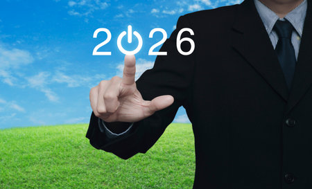 Businessman pressing 2026 start up business flat icon over green grass field with blue sky, Business happy new year 2026 success conceptの写真素材