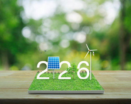 2026 white text with solar cell, wind turbine and growing tree on green grass on open book on wooden table over blur tree in park, Happy new year 2026 green ecology and saving energy conceptの写真素材