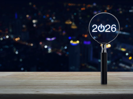 2026 start up flat icon with magnifying glass on wooden table over blur colorful night light modern city tower and skyscraper, Business happy new year 2026 success conceptの写真素材