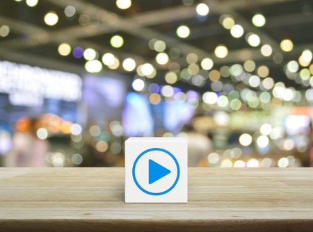Play button flat icon on white block cube on wooden table over blur light and shadow of shopping mall, Business music online conceptの写真素材