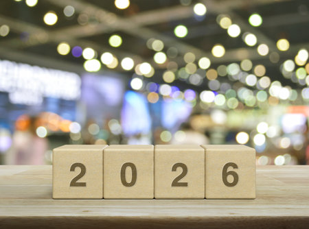 2026 letter on wood block cubes on wooden table over blur light and shadow of shopping mall, Happy...