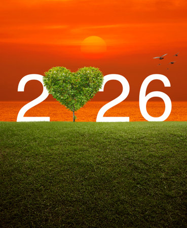 Tree in the shape of heart love with 2026 white text on green grass field over sunset sky and sea,...