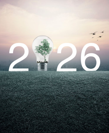 2026 white text and light bulb with tree inside on green grass field over aerial view of cityscape at sunset, vintage style, Happy new year 2026 green ecology and saving energy conceptの写真素材
