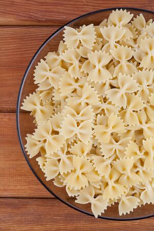 Raw farfalle in glass plate on wooden boardの写真素材