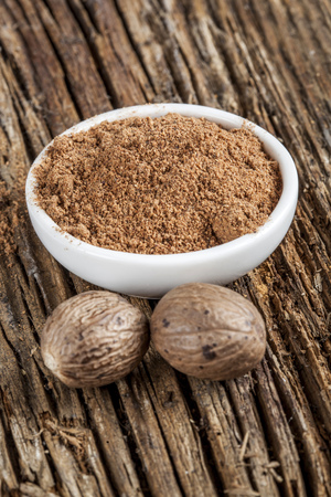 Spice nutmeg in whole and ground in a white bowlの写真素材