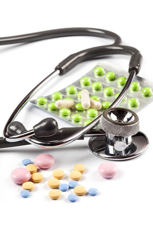 Multi color pills spills around the stethoscope, one blister with green pills, isolated on whiteの写真素材