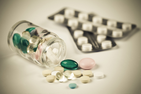 Medical pills shedding of a transparent bottle, two blisters in the background, old style colorsの写真素材