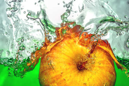 Yellow apple  moving in real green  water with a splash and drops of water on a close-upの写真素材