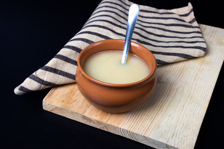 Pure cow ghee in ceramic bowl on black background with ghee spoon in handの写真素材