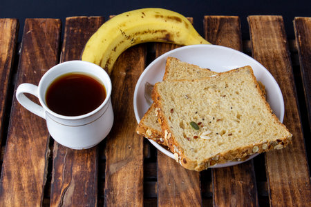Healthy tasty morning breakfast with multigrain bread black coffee and banana on woodenの写真素材