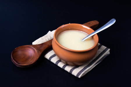 Pure cow ghee in ceramic bowl on black background with ghee spoon in handの写真素材