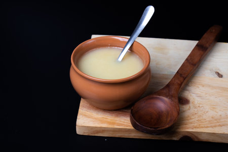Pure cow ghee in ceramic bowl on black background with ghee spoon in handの写真素材