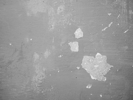 Peeling paint on a wall, revealing a textured surface with scattered light and dark spots.の写真素材