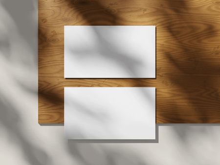 Top view of two business cards on a wooden table with soft lighting and shadows.の写真素材