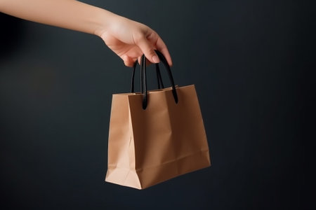 cropped view of woman holding brown paper shopping bag isolated on blackの素材