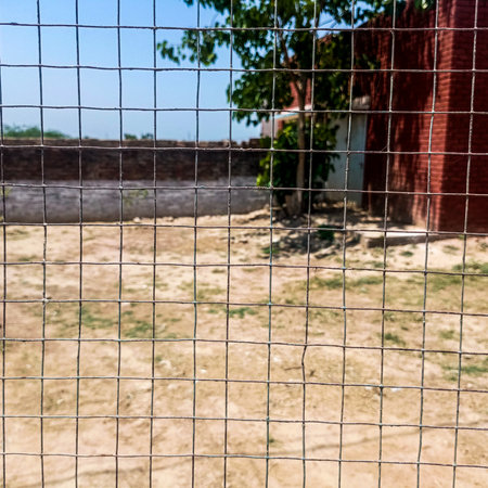 Wire mesh fence on the background of the brick wall and blue skyの写真素材