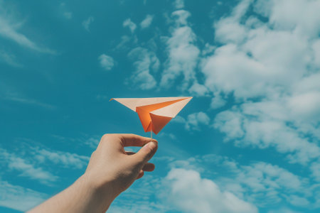 Paper airplane in hand on blue sky background with white clouds, retro tonedの素材