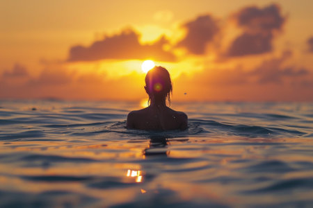 Silhouette of a beautiful young woman in the water at sunsetの素材
