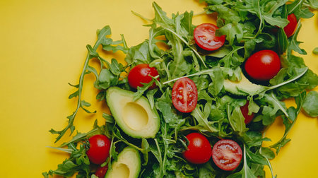 Fresh salad with avocado, cherry tomatoes and arugula on yellow backgroundの写真素材
