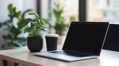 Laptop with blank screen on wooden table in modern office. Workplace with laptop and coffee cup.