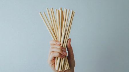 Female hand holding a bunch of bamboo straws on a gray backgroundの写真素材