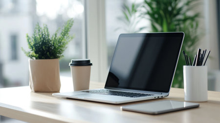 Close up of modern workplace with blank screen laptop, coffee cup and plant in pot on wooden table
