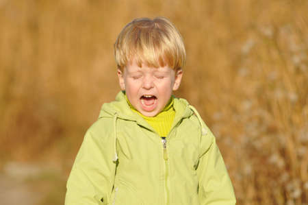 Crying blond boy portrait in green jacket outdoor