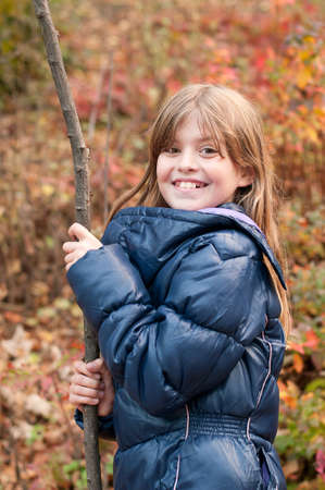 Pretty nine years girl with stick outdoor in autumn smiles and looking at cameraの写真素材