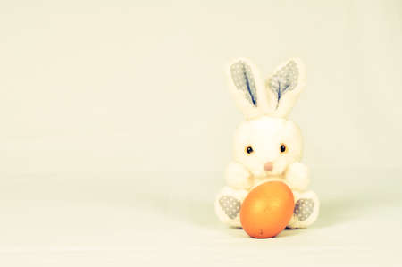 Toy fluffy easter bunny with orange egg sits on white background and lookinga at camera. There is copy space.の写真素材