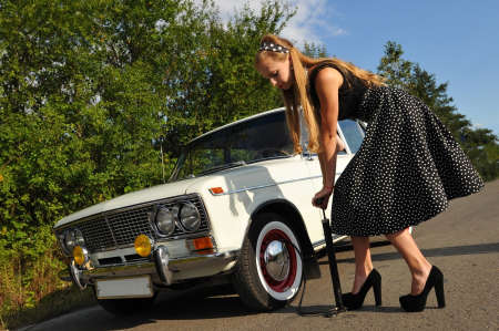 Pretty young woman outdoor at summer trying to pump tyre of white old carの写真素材
