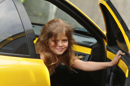 Pretty girl open door of yellow sport car and looking at camera. She is seven years old and have long haird down.の写真素材