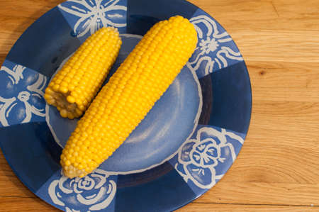 Yellow boiled ear corn on blue plate with flower patternの写真素材