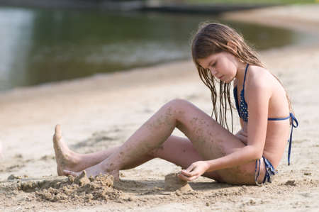 Eleven years girl pretty girl plays with sand on the beachの写真素材