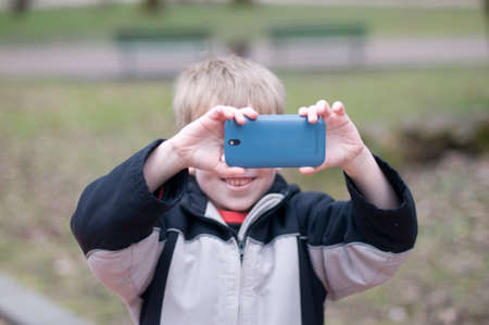 Little boy taking photos on smartphone in parkの写真素材