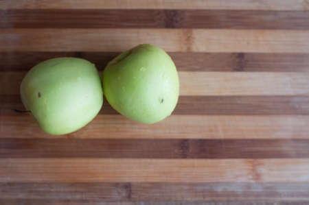 Two green apples lie on wooden cutting boardの写真素材